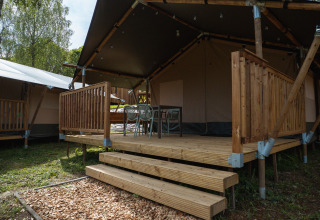 Safaritent met houten terras en stoelen bij Hameau de l'Ourthe in België, tussen het groen gelegen.