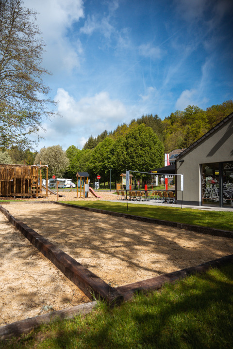 Tente safari au Hameau de l'Ourthe en Belgique avec aire de jeux, bac à sable et arbres verdoyants.