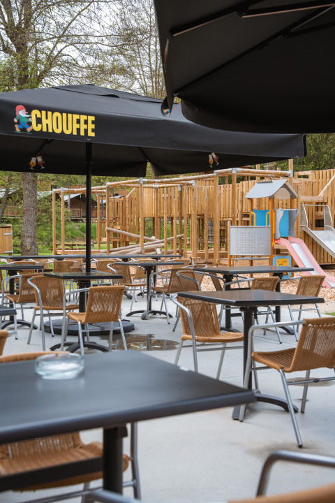Terrasse de café extérieure avec tables vides et aire de jeux, à Safari Tent, Hameau de l'Ourthe, Belgique.