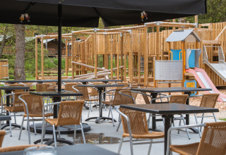 Udendørs caféområde med tomme stole og borde, legeplads i baggrunden ved Safari Tent, Hameau de l'Ourthe.