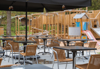 Buitenterras met stoelen en tafels, speeltuin zichtbaar bij Safari Tent in Hameau de l'Ourthe, België.