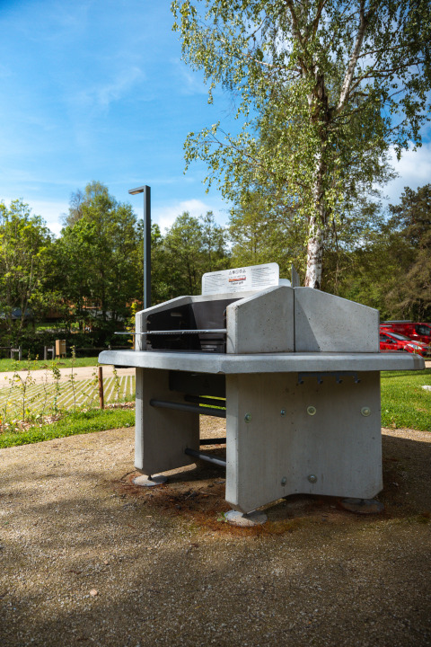 Espace barbecue extérieur au Safari Tent, entouré d'arbres et d'un parking sous un ciel bleu et ensoleillé.