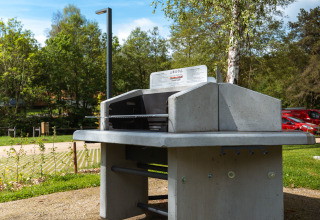 Openluchtbarbecue bij Safari Tent met bomen en parking op de achtergrond onder een blauwe hemel.