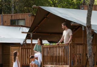 Familie nyder en solrig dag udenfor en safaritelte på Hameau de l'Ourthe i Belgien med træer omkring.