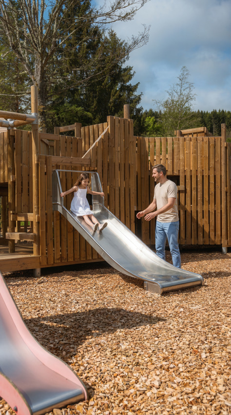 Un homme accompagne une enfant sur un toboggan au terrain de jeux du Safari Tent à Hameau de l'Ourthe, Belgique.