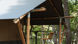 Safaritent met houten terras en twee stoelen tussen de bomen, gelegen in een weelderig bos.