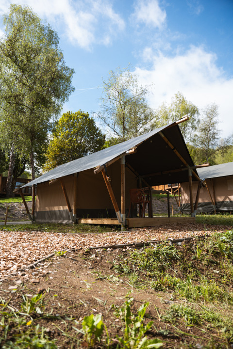 Safaritent bij Hameau de l'Ourthe in België, omringd door bomen en blauwe lucht, ideaal voor glamping.