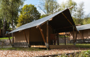 Safaritent bij Hameau de l'Ourthe in België, omringd door bomen en blauwe lucht, ideaal voor glamping.