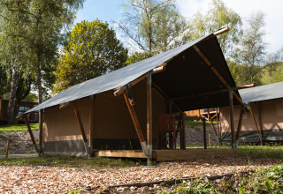 Safari-telt ved Hameau de l'Ourthe i Belgien, omgivet af træer og blå himmel, ideelt til glamping.