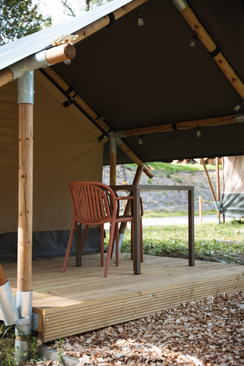 Safari tent at Hameau de l'Ourthe in Belgium with wooden deck, brown chair, and table for outdoor seating.