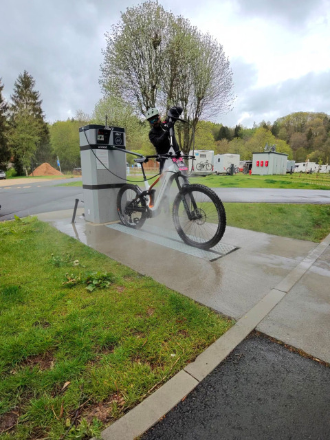 Person washing their mountain bike with a pressure washer at a dedicated bike wash station on a campsite.