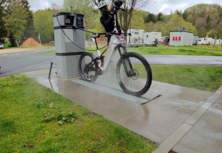 Person washing their mountain bike with a pressure washer at a dedicated bike wash station on a campsite.