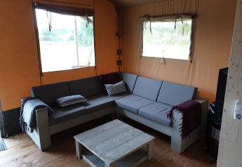 Indvendig udsigt af en safari-teltstue med en grå hjørnesofa, sofabord og vinduer på Camping Gorishoek.