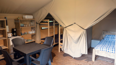 Binnenkant van een safaritent op Camping Emmen in Nederland met slaapgedeelte, tafel en keukenkastjes.