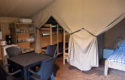 Interior de una tienda safari en Camping Emmen, Países Bajos, con zona de dormir, mesa y cocina equipada.