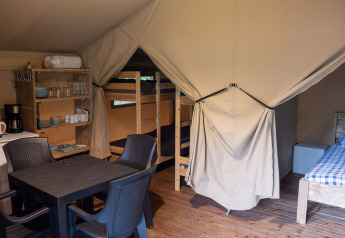 Interior of a safari tent at Camping Emmen, Netherlands, showing sleeping areas, kitchen, and dining table.