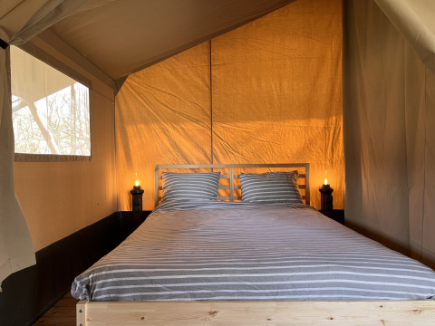 Interior of a safari tent at Camping 'de Val' with double bed, striped bedding, and warm lighting.