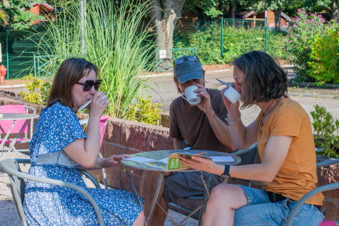 Drie mensen aan een tafeltje buiten, genietend van drankjes op Onlycamp Camping l'Orée d'Alsace.