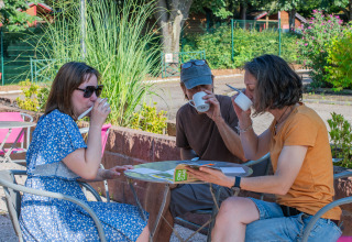 Drei Personen genießen gemeinsam Getränke an einem Tisch im Freien bei Onlycamp Camping l'Orée d'Alsace.