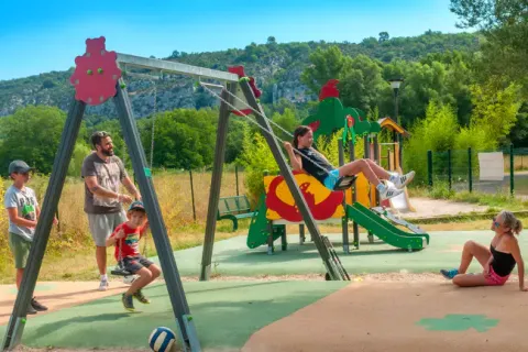 Kinder und Erwachsene spielen auf einem Spielplatz mit Schaukeln im Seasonova Camping Les Prés du Verdon.