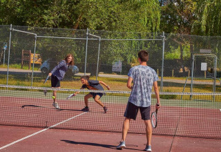 Three people are playing tennis on an outdoor court surrounded by trees at Seasonova Camping Les Prés du Verdon.