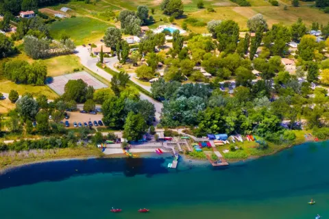 Luchtfoto van Seasonova Camping Les Prés du Verdon met bomen, huisjes en een oever in Frankrijk.