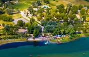 Aerial view of Seasonova Camping Les Prés du Verdon in Provence, with lakeside, trees, and cabins.