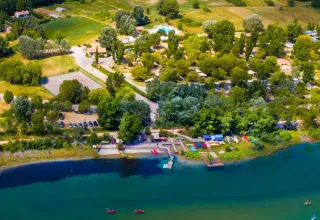 Aerial view of Seasonova Camping Les Prés du Verdon in Provence, with lakeside, trees, and cabins.