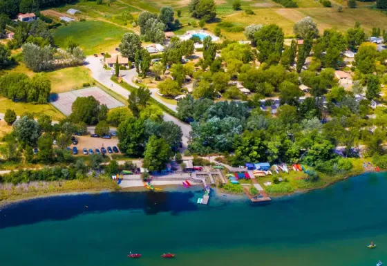 Luchtfoto van Seasonova Camping Les Prés du Verdon met bomen, huisjes en een oever in Frankrijk.