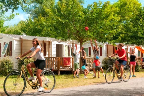 Familier nyder ferie i Seasonova Camping Les Prés du Verdon med cykling og leg blandt mobilhomes i solen.