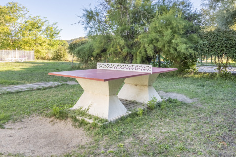 Tischtennisplatte im Freien aus Beton, umgeben von Bäumen und Wiese im Seasonova Camping Les Prés du Verdon.