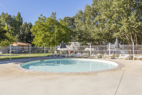 Runder Pool mit Liegestühlen und Sonnenschirmen im Seasonova Camping Les Prés du Verdon, umgeben von Grün.