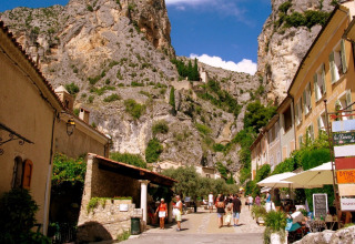 Billedet viser en malerisk gade i Quinson, Provence-Alpes-Côte d’Azur med klipper i baggrunden.