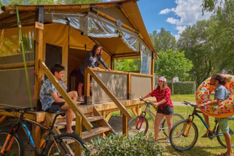 Vier Personen entspannen vor einem Comfort Lodge Safarizelt mit Fahrrädern und Schwimmreifen im Grünen.