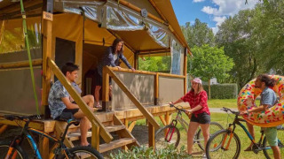 Quattro persone si godono l’esterno vicino a una tenda safari Comfort Lodge con bici e ciambella gonfiabile.