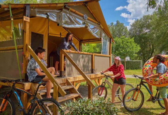 Vier Personen entspannen vor einem Comfort Lodge Safarizelt mit Fahrrädern und Schwimmreifen im Grünen.
