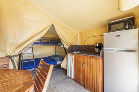 Interieur van Comfort Lodge safari tent met keuken, stapelbedden, eettafel en kasten op een camping.