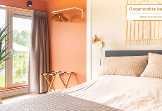 Slaapkamer in Tiny House XL bij De Kremmer, Nederland, met comfortabel bed, grote ramen en moderne warme inrichting.
