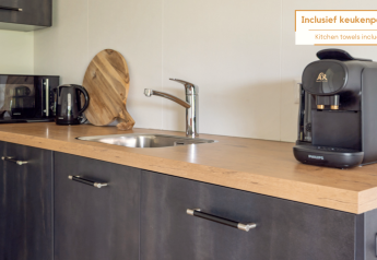 Petite cuisine d'une tiny house avec cafetière, micro-ondes, bouilloire, évier et planche à découper.