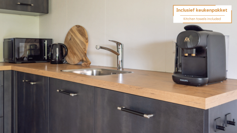 Compact kitchenette in a tiny house with a coffee maker, microwave, kettle, sink, and cutting board.