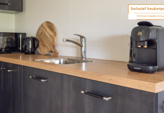 Compact kitchenette in a tiny house with a coffee maker, microwave, kettle, sink, and cutting board.