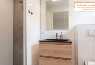 Modern bathroom in a tiny house with shower, wooden sink cabinet and large mirror. Towels are included.
