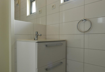 Moderne badeværelse med hvidt vaskeskab, vinduer og flisevæg i Adventure Lodge, Bloemendaal aan Zee.