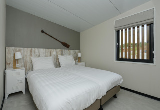 Chambre moderne avec lits jumeaux, décoration rame murale et fenêtre au Sea House Comfort aux Pays-Bas.