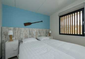 Soveværelse i Sea House Special-lodge, Bloemendaal aan Zee, med to senge, blå væg og årer som dekoration.