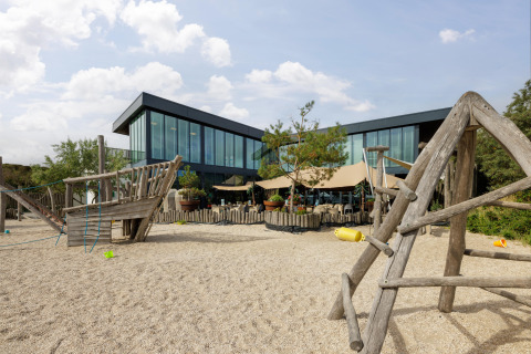 Parco giochi con strutture in legno davanti a un edificio moderno al villaggio turistico Bloemendaal aan Zee.
