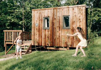 To børn leger bold foran en trætinyhouse kaldet Ecolodge ved Hameau de l'Ourthe i Belgien.