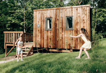 Twee kinderen spelen met een bal bij het houten Ecolodge tiny house in Hameau de l'Ourthe, België.