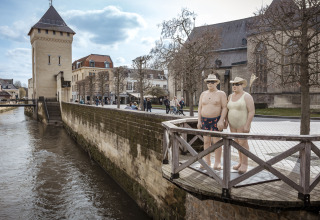 Twee realistische beelden in badpak op een balkon langs een rivier in een schilderachtig stadje.