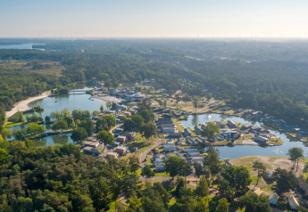 Vue aérienne d’un site de glamping entouré de forêts, avec des cabanes situées près de lacs paisibles.